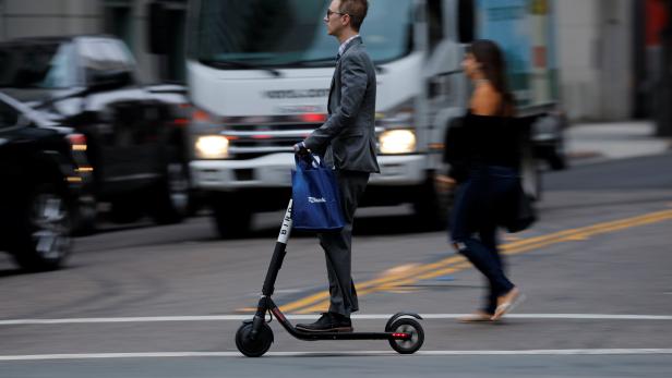 A man in a suit rides an electric BIRD rental scooter along a city street in San Diego, California