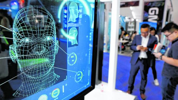 Visitors check their phones behind the screen advertising facial recognition software during Global Mobile Internet Conference (GMIC) at the National Convention in Beijing