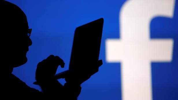 FILE PHOTO: A man is silhouetted against a video screen with an Facebook logo in this photo illustration in Zenica
