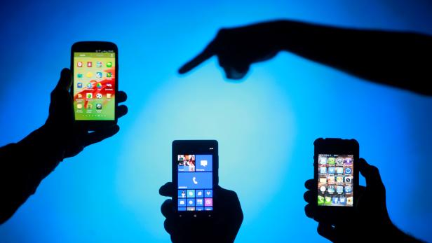 FILE PHOTO: Men are silhouetted against a video screen as they pose with smartphones