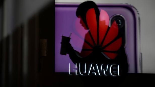 A man walking past a Huawei P20 smartphone advertisement is reflected in a glass door in front of a Huawei logo, at a shopping mall in Shangha
