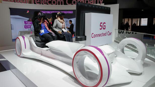 Women sit in a 5G connected car simulator displayed at the Saudi Telecom Company stand during the Mobile World Congress in Barcelona