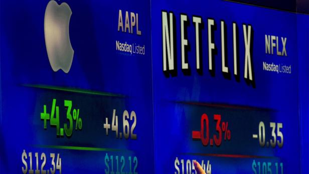 A reporter points at ticker symbols for Apple Inc. and Netflix displayed on a screen at the Nasdaq Market site in New York