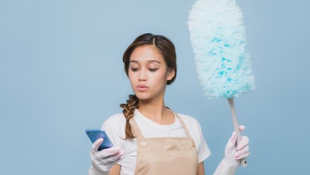 Young woman watching smart phone while house cleaning while cleaning.