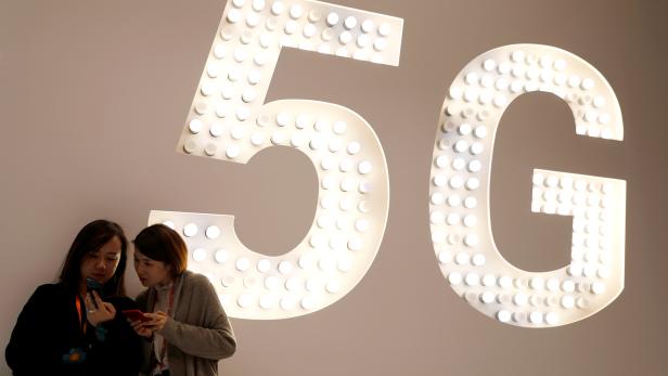 Visitors use their mobiles phones as they stand next to a 5G Led Smart Bulb panel inside the Xiaomi booth at the Mobile World Congress in Barcelona