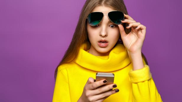 Portrait surprised young girl from message on smartphone in brightly yellow sweater, isolate on a violet background