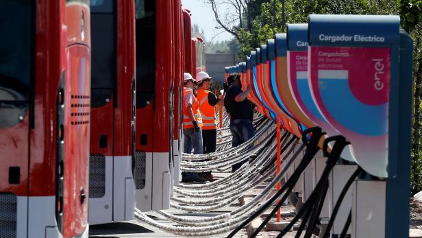 Men supervise the electric chargers for the new fleet of electric buses for public transport manufactured by China's BYD, in a bus terminal in Santiago