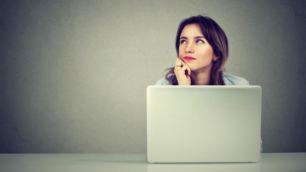 young business woman thinking daydreaming sitting at desk with laptop computer