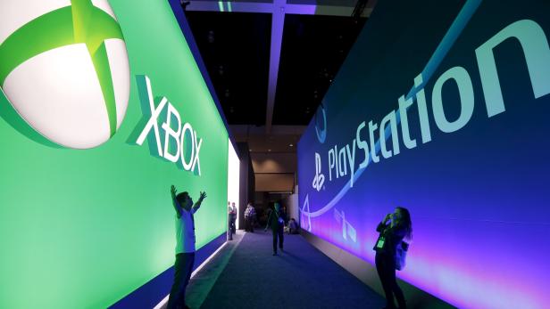 A man poses for a photo in front of a Microsoft Xbox sign opposite a Sony PlayStation sign at the Electronic Entertainment Expo, or E3, in Los Angeles