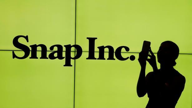 FILE PHOTO: A woman stands in front of the logo of Snap Inc. on the floor of the New York Stock Exchange (NYSE) while waiting for Snap Inc. to post their IPO, in New York City