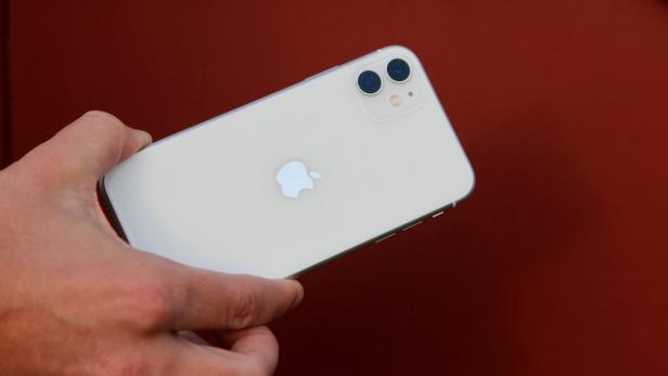 Eine Hand hält ein weißes iPhone vor einem roten Hintergrund.