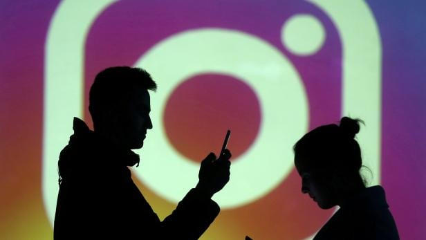 FILE PHOTO: Silhouettes of mobile users are seen next to a screen projection of Instagram logo in this picture illustration
