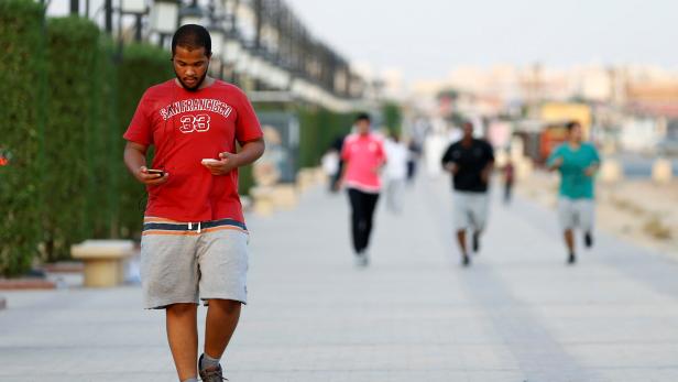 A Saudi man uses his smartphone as he walks on a sidewalk in Riyadh