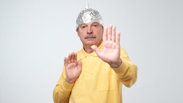 Caucasian mature man in a tin foil hat displeased closing his face with hands.