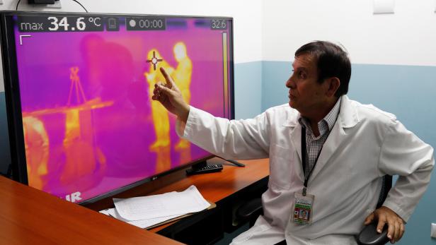 A doctor points to a monitor showing thermal scanners that detect temperatures of passengers at the security check inside the airport in Guatemala City