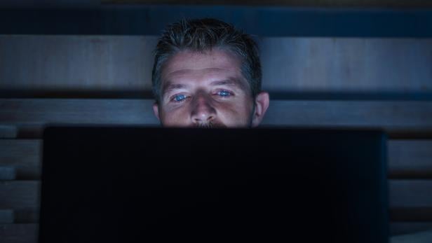 young attractive and relaxed internet addict man networking concentrated late at night on bed with laptop computer in social media addiction or workaholic businessman concept