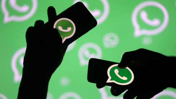 FILE PHOTO: Men pose with smartphones in front of displayed Whatsapp logo in this illustration