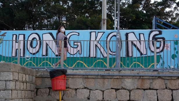 Woman wearing a face mask walks past a graffiti reading "Hong Kong" on a beach at Cheung Chau island during Easter weekend, amid the novel coronavirus disease (COVID-19) outbreak
