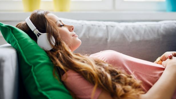 Portrait of a beautiful young woman lying on sofa with headphones on and closed eyes, relaxing