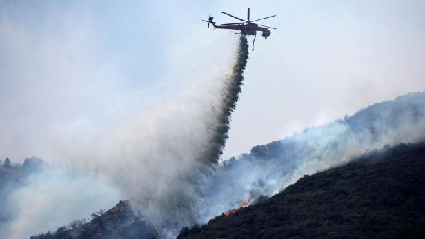 A helicopter makes a water drop over a wildfire in the Angeles National Forest during the Bobcat Fire in Los Angeles