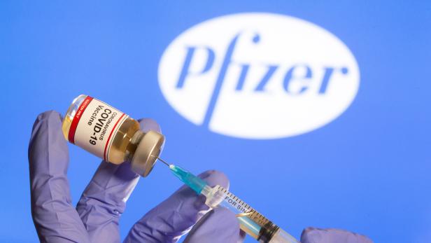 FILE PHOTO: A woman holds a small bottle labeled with a "Coronavirus COVID-19 Vaccine" sticker and a medical syringe in front of displayed Pfizer logo in this illustration