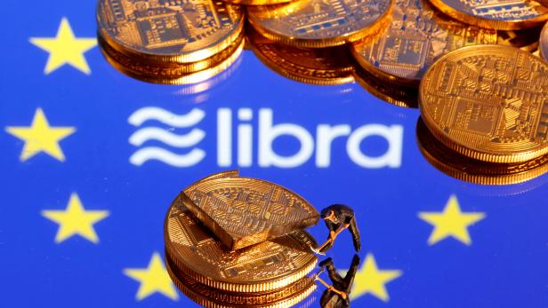 FILE PHOTO: A small toy figure is seen on representations of the virtual currency on a displayed European Union flag and the Facebook Libra logo in this illustration picture