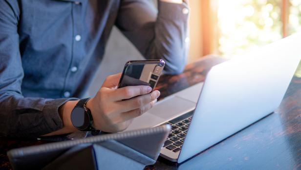 Male hand holding smartphone. Businessman using laptop computer and digital tablet while working in the cafe. Mobile app or internet of things concepts. Modern lifestyle in digital age.