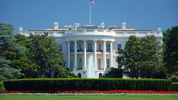 Das Weiße Haus mit amerikanischer Flagge unter blauem Himmel.