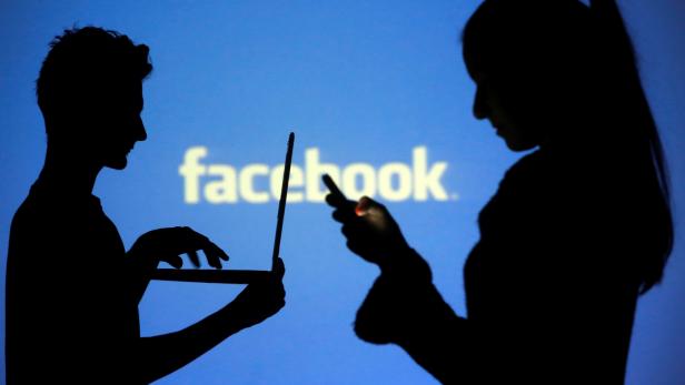 FILE PHOTO: People pose with laptops in front of projection of Facebook logo in this picture illustration taken in Zenica