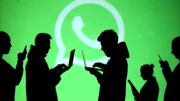 FILE PHOTO: Silhouettes of laptop and mobile device users are seen next to a screen projection of Whatsapp logo in this picture illustration