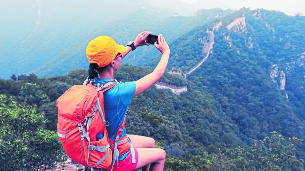 young woman hiker taking photo with smart phone on top of great wall