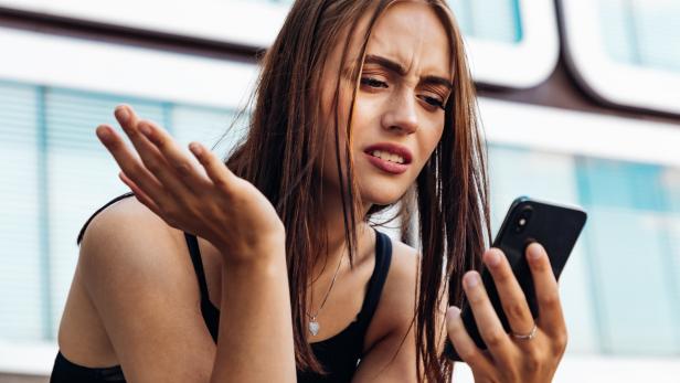Eine junge Frau schaut verärgert auf ihr Smartphone.
