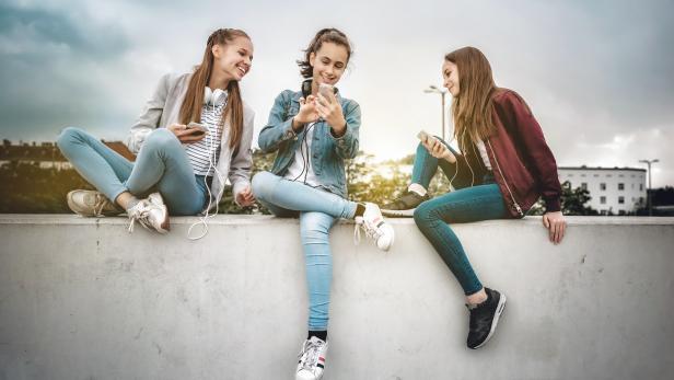three teenage girls with smartphones on concrete wall