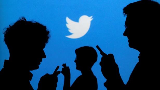 FILE PHOTO: FILE PHOTO: People holding mobile phones are silhouetted against a backdrop projected with the Twitter logo  in Warsaw