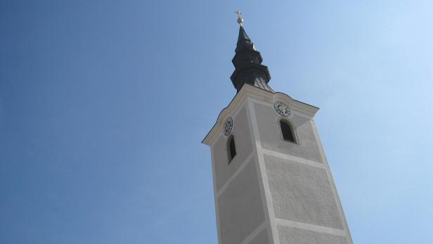 Ein weißer Kirchturm ragt in den blauen Himmel