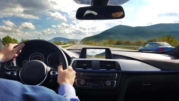 Blick aus dem Inneren eines Autos auf eine Autobahn mit Bergen im Hintergrund.