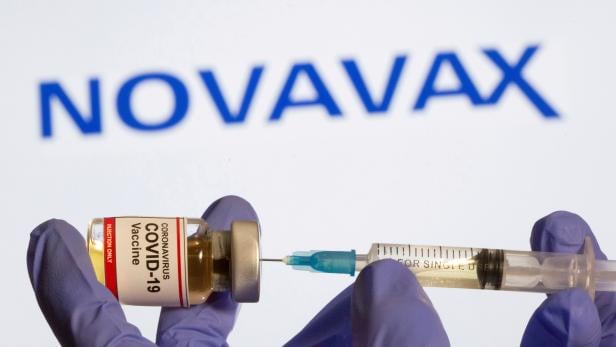FILE PHOTO: FILE PHOTO: A woman holds a small bottle labeled with a "Coronavirus COVID-19 Vaccine" sticker and a medical syringe in front of displayed Novavax logo in this illustration