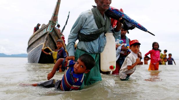 FILE PHOTO: A Rohingya refugee man pulls a child as they walk to the shore after crossing the Bangladesh-Myanmar border by boat through the Bay of Bengal in Shah Porir Dwip