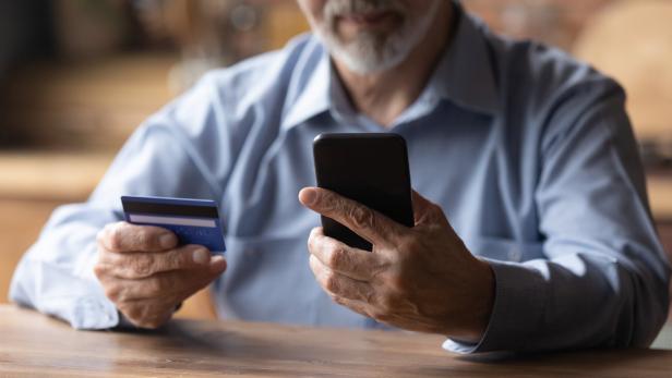 Ein älterer Mann benutzt sein Smartphone und hält eine Kreditkarte in der Hand.