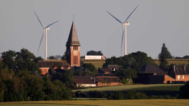 Two power-generating windmill turbines are seen behind the church of the village in Ruyaulcourt