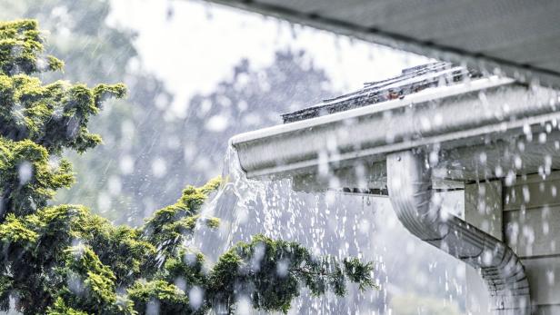 Regenwasser fließt von einem Dach in eine Dachrinne.