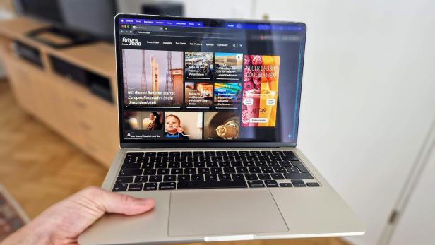 Ein MacBook wird in der Hand gehalten und zeigt die Webseite futurezone.at.