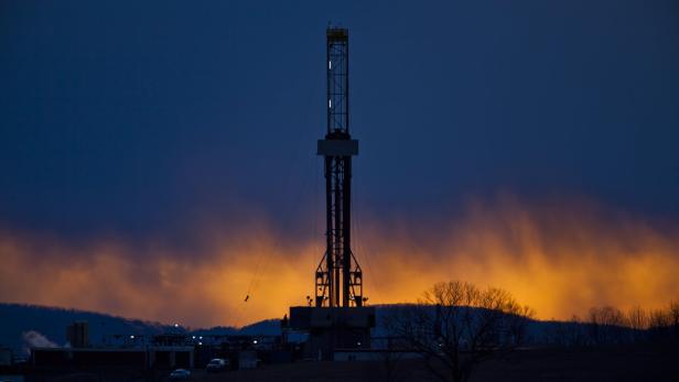 Ein Ölbohrturm steht vor einem orangefarbenen Himmel in der Abenddämmerung.