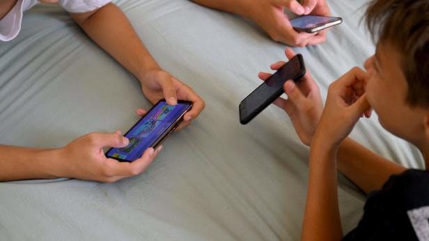 Drei Jugendliche liegen auf einem Bett und benutzen ihre Smartphones.