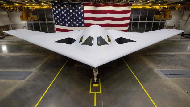 Ein B-21 Raider Tarnkappenbomber steht vor einer großen US-Flagge.