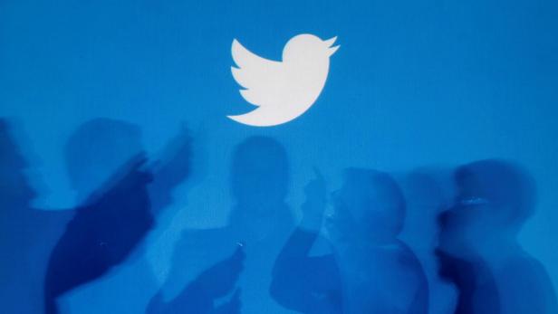 FILE PHOTO: Shadows of people holding mobile phones are cast onto a backdrop projected with the Twitter logo  in Warsaw