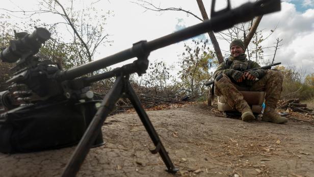 Ukrainian serviceman Yuriy smiles next to a machine gun at a position on a frontline in Mykolaiv region