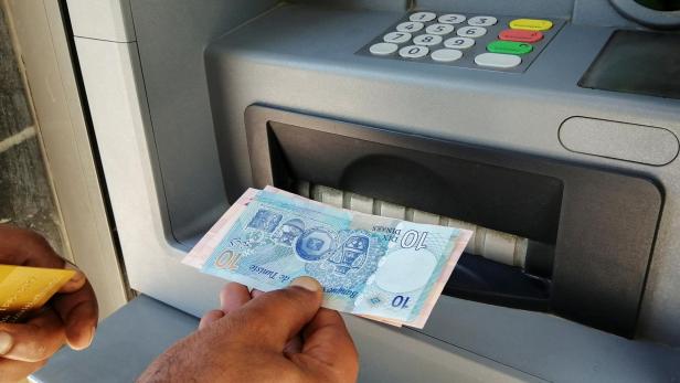 FILE PHOTO: A man displays Tunisian dinar banknotes after withdrawing cash from an ATM machine in Tunis