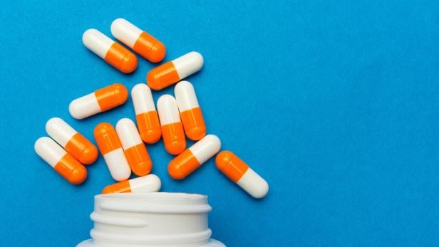 Orange white capsules (pills) were poured from a white bottle on a blue background. Medical background, template.