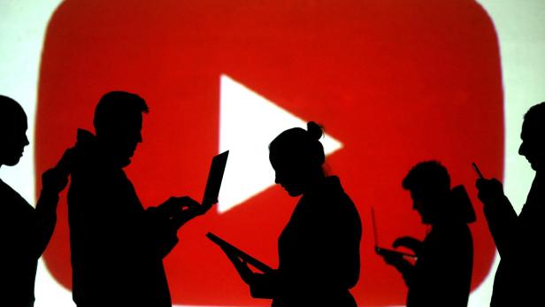 FILE PHOTO: Silhouettes of laptop and mobile device users next to a screen projection of the YouTube logo in this picture illustration